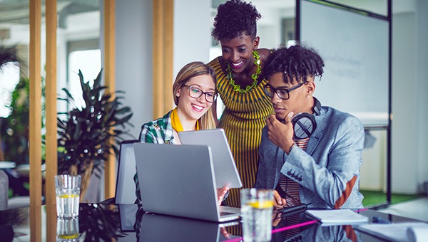 年轻的员工们聚集在一台笔记本电脑周围，在一个项目上合作